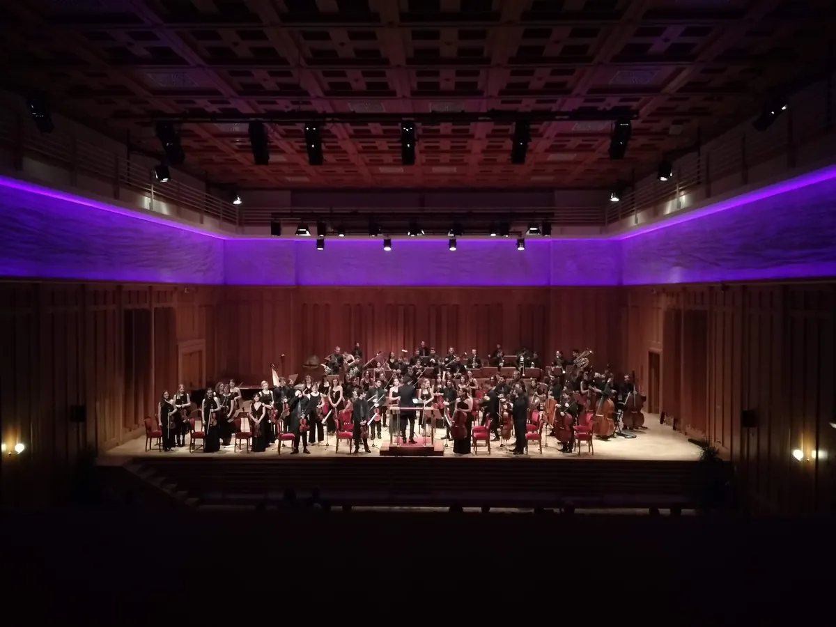 A full orchestra on the platform of a modern concert hall