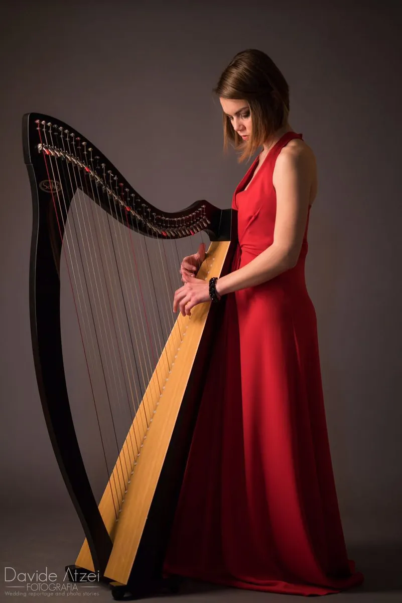 Eleonora Congiu, harpist, standing at a lever harp in a red concert dress