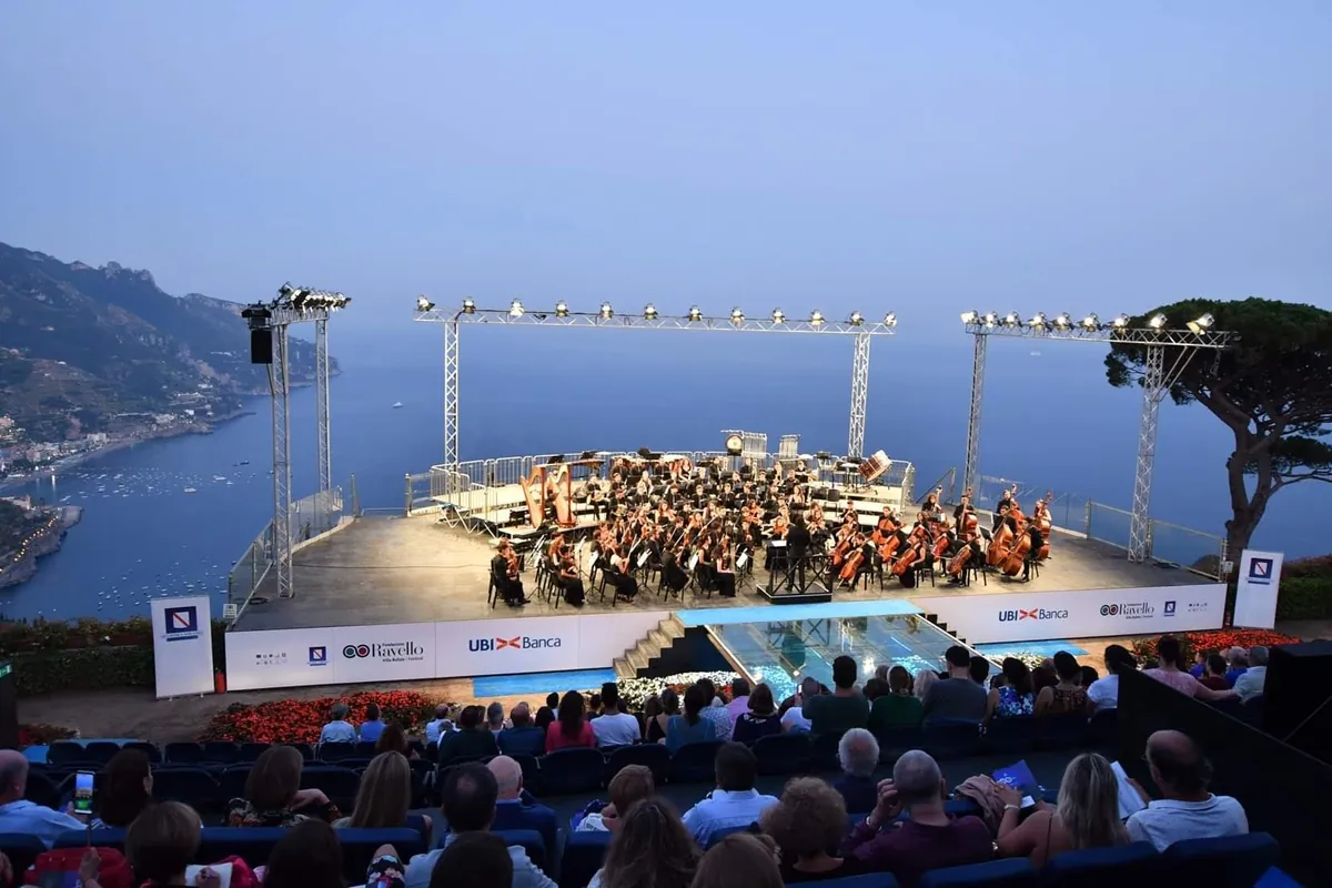 An orchestra on the open-air stage at Ravello above the sea at dusk