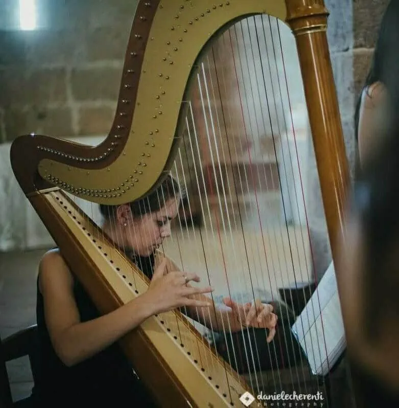 Eleonora Congiu playing the pedal harp in a stone-walled church