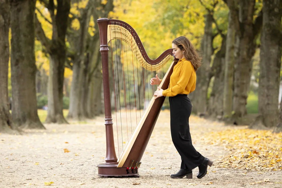 Eleonora Congiu playing her pedal harp outdoors on a path lined with autumn trees