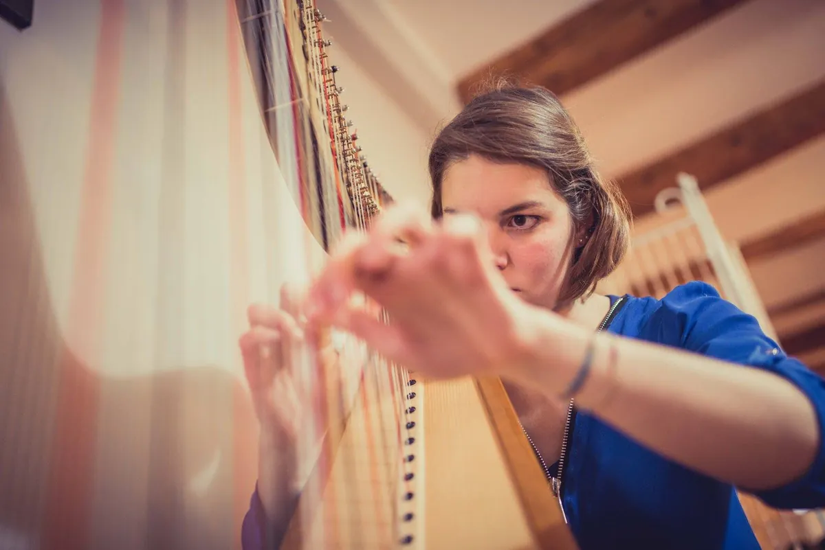Eleonora Congiu playing the pedal harp mid-phrase, light falling across the strings