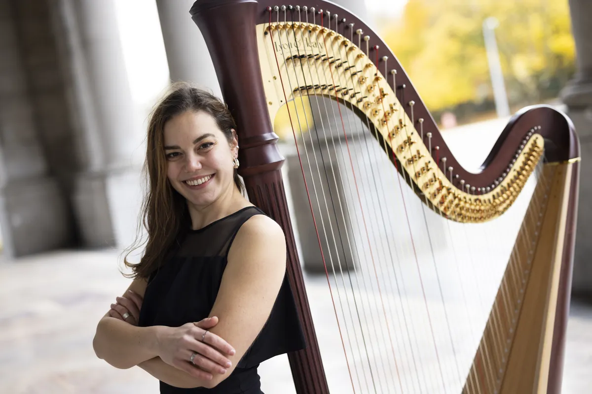 Eleonora Congiu smiling with her arms crossed beside her pedal harp