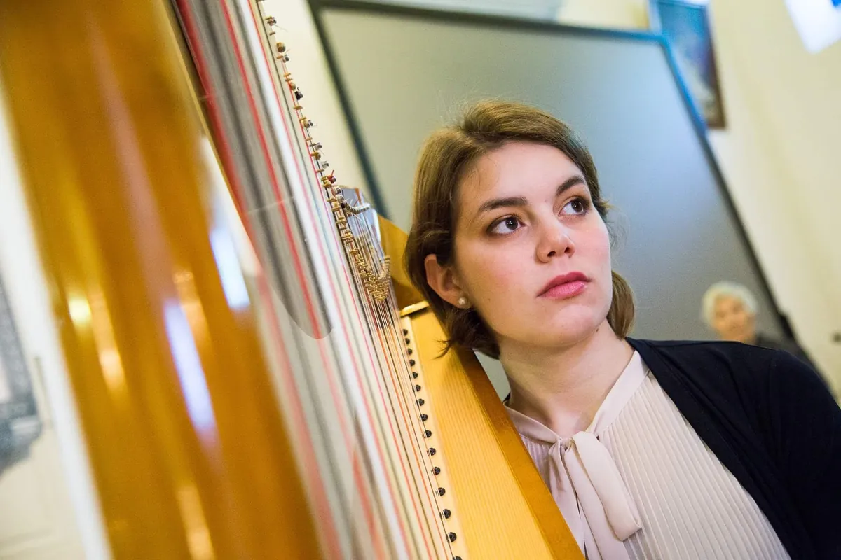 Eleonora Congiu resting against the column of her pedal harp, looking past the camera