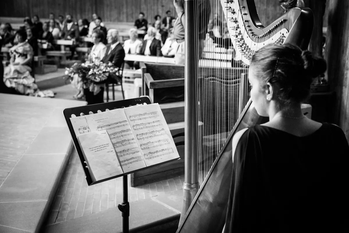 Eleonora Congiu at the harp seen from behind, with a seated audience in front of her
