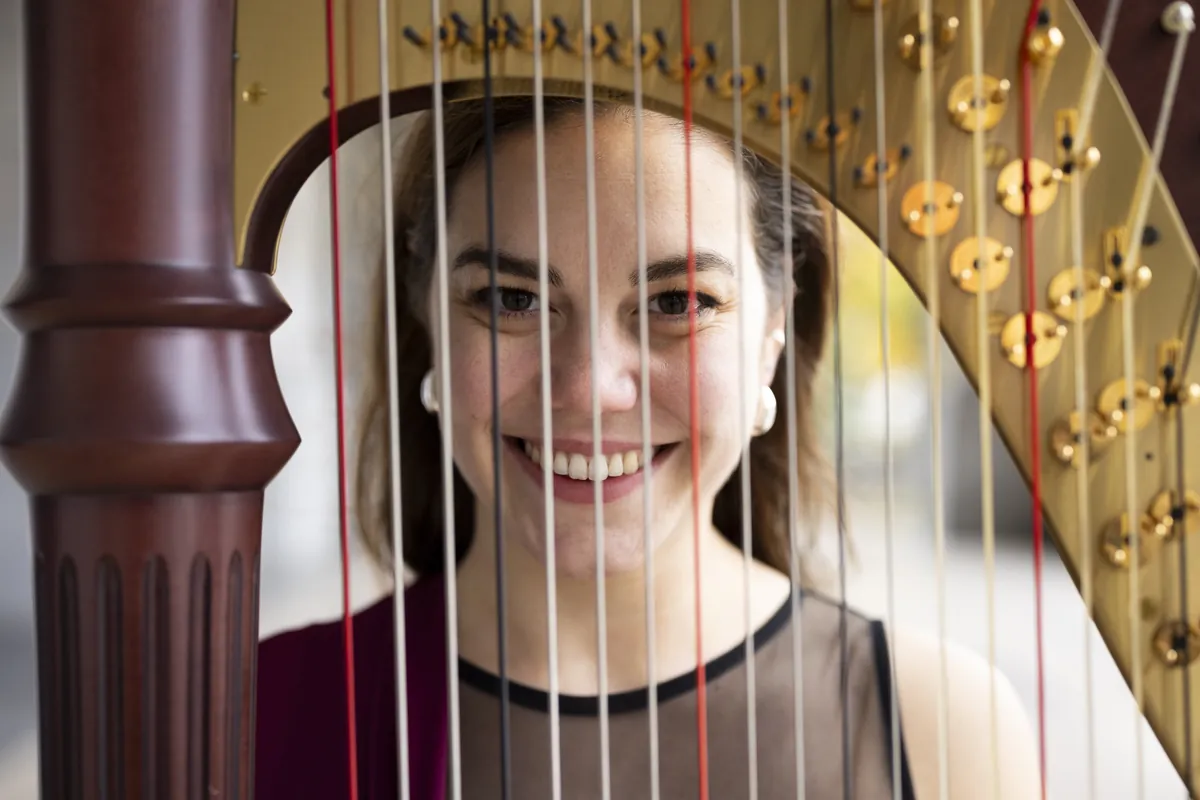 Eleonora Congiu smiling, framed between the strings of her pedal harp
