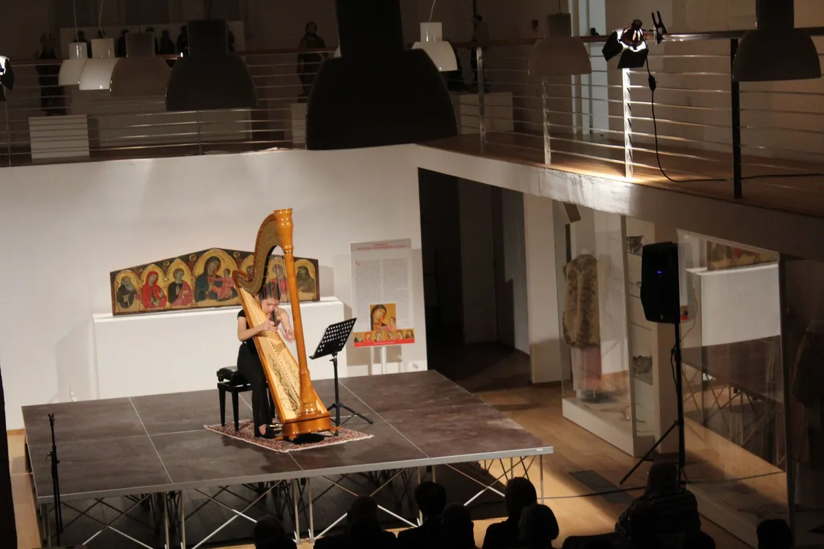 Eleonora Congiu playing a solo harp recital on a museum stage with medieval altarpieces behind her