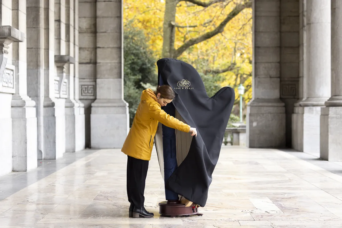 Eleonora Congiu lifting the padded cover from her pedal harp under a stone colonnade